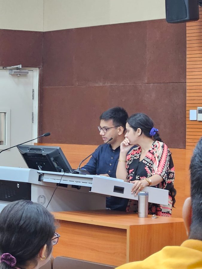 Two people at the lectern console of an auditorium, one on a headset microphone