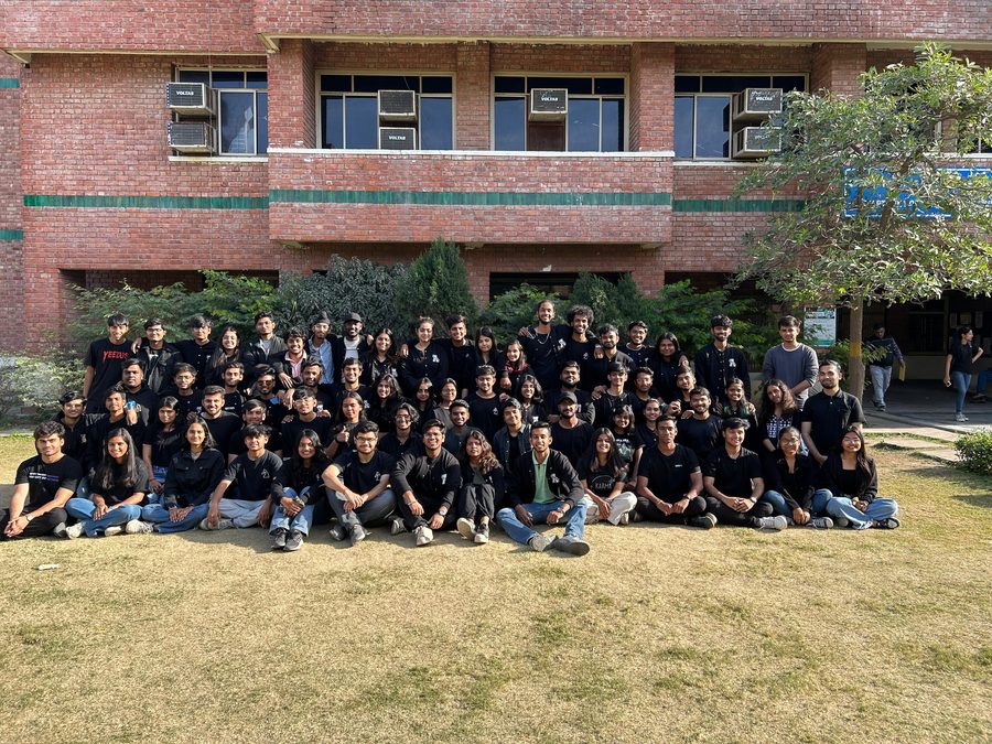 About seventy students in black t-shirts arranged on the lawn in front of a brick academic block